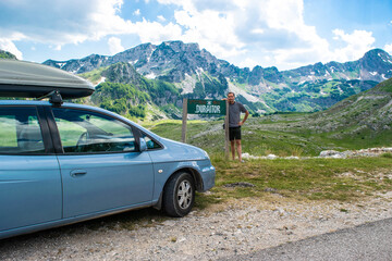 Fototapeta na wymiar Man tourist near sign with the inscription Durmitor and car on background mountains Durmitor National Park. Montenegro.
