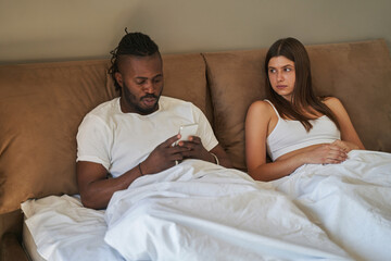 Sad woman staring at man focused on his cellphone