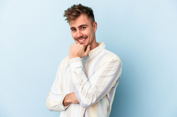 Young caucasian man isolated on blue background smiling happy and confident, touching chin with hand.