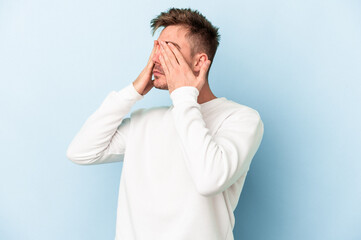 Young caucasian man isolated on blue background afraid covering eyes with hands.