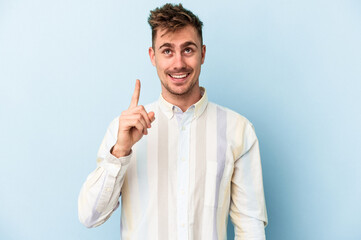Young caucasian man isolated on blue background indicates with both fore fingers up showing a blank...