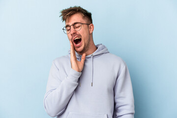 Young caucasian man isolated on blue background yawning showing a tired gesture covering mouth with hand.