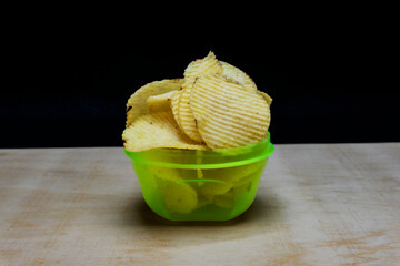 Salted Potato Chips Wafers in lite Green bowl on table, isolated in black background, Heap of Chips...
