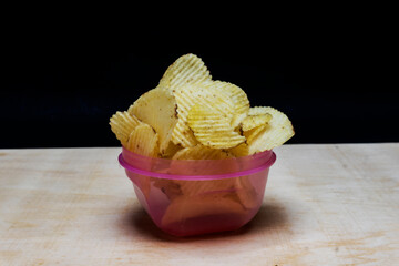 Salted Potato Wafers in lite pink bowl on table, isolated in black background, Heap of Wafers