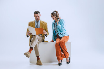 Portrait of young happy family, man and woman in retro style clothes, fashion of 70s, 60s years sitting together isolated on white studio background