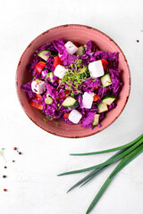 Salad with red napa cabbage, feta cheese, bell pepper and cucumber in the ceramic bowl topped with microgreen on the white table. Healthy meal. Top view