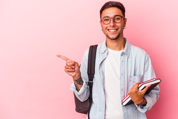 Young caucasian student man holding books isolated on pink background  smiling and pointing aside,...