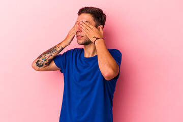 Young caucasian man with tattoos isolated on yellow background  afraid covering eyes with hands.