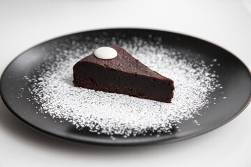 Dark chocolate brownie decorating with icing sugar on black dish