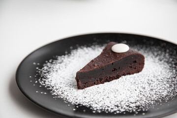 Dark chocolate brownie decorating with icing sugar on black dish