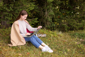 Fototapeta premium Young woman working on laptop in forest, space for text