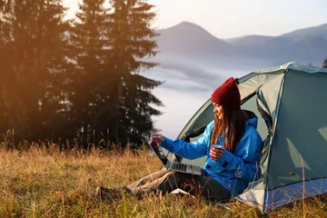  Woman working on laptop near camping tent outdoors surrounded by beautiful nature © New Africa