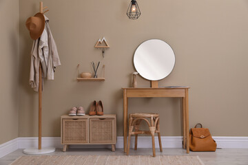 Modern hallway interior with stylish furniture, round mirror and wooden hanger for keys on beige...