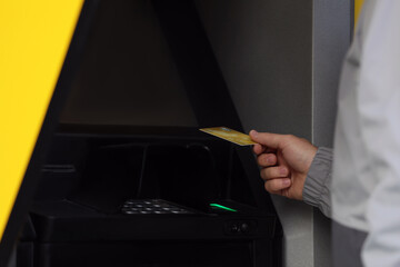 Obraz premium Man with debit card using cash machine for money withdrawal outdoors, closeup