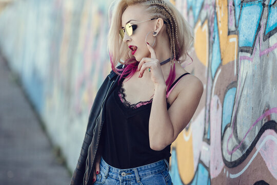 Portrait of young woman with piercings and tattoos against graffiti wall.