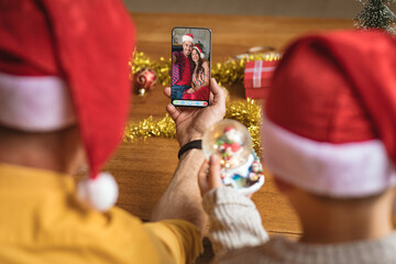 Father and son in santa hats making smartphone christmas video call with caucasian couple