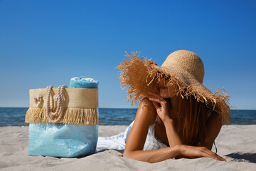 Woman with beach bag and straw hat lying on sand near sea © New Africa