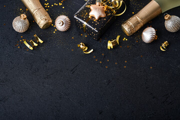 Christmas or New Year concept. Holiday gift box or present with ribbon, champagne, golden confetti and gold baubles on black background.  Christmas  card. Christmas Decoration. Mock up. Top view.