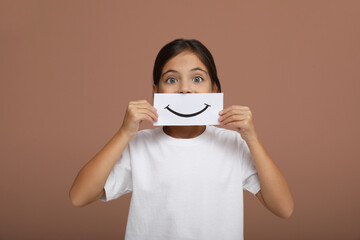 Little girl holding sheet of paper with smile on pale pink background