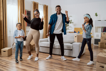 Fototapeta premium A happy family dances in the middle of the living room, young parents and their children celebrate moving into a new apartment, rejoice together, practice choreography