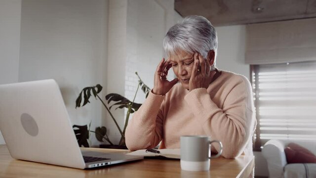 Multi-cultural elderly female concerned, recieving bad news while on laptop, sitting at kitchen counter