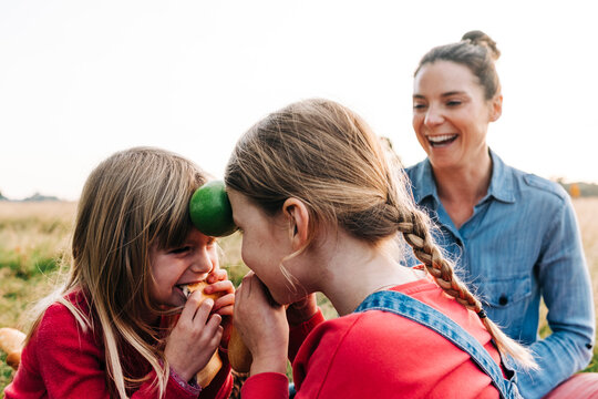 Playful Girls With Face To Face Holding Fruit And Eating Bread At Park