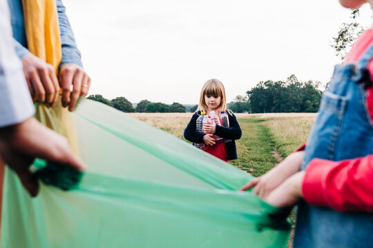 Girl Collecting Plastic Bottles With Family In Park