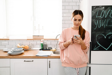 White ginger woman using mobile phone while standing in kitchen