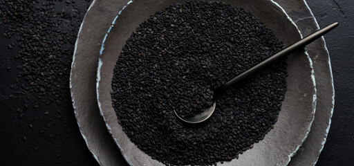 Black sesame seeds in black ceramic plates on a dark old vintage background. Rustic style. Top view