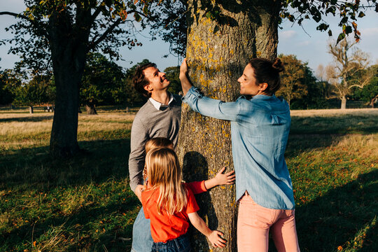 Parents and daughters embracing tree in park on weekend