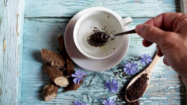Healthy coffee substitute infusion made with chicory root, the root, the flower and a cup are displayed on a bluish wooden background