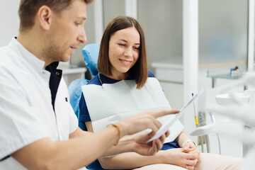 Male Professional Dentist With Gloves And Mask Holding papers photo And Show What The Treatment Will Look Like Of The Patient's Teeth. Discussion Of The Treatment Plan And Healthy Smile