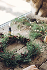 Woman making Christmas wreath by attaching red berries to fir tree branch during Christmas workshop, Handmade advent wreath creation process concept