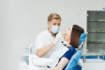 Fototapeta na wymiar Caucasian male dentist examining young woman patient's teeth at dental clinic. Doctor probing teeth with dental instrument using an explorer look for cavities treatment and checking problems