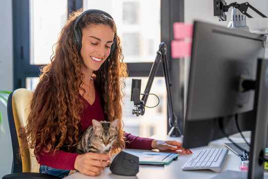 Smiling young woman looking at cat on desk