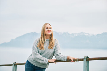 Outdoor portrait of happy beautiful young woman relaxing in mountains over the clouds, wearing grey pullover
