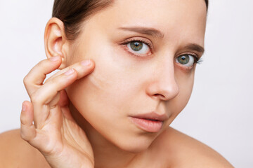 Close-up of a young beautiful caucasian woman touching the face with her hand applying a cream on the skin isolated on a white background. Nourishing moisturizing cream. Cosmetology and beauty concept