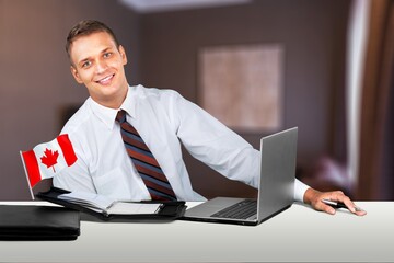 Happy young guy sitting with flag of Canada, using a laptop computer