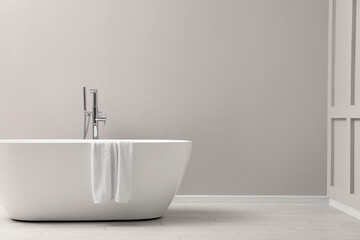Naklejka na ściany i meble Modern ceramic bathtub with towel near light wall indoors, space for text