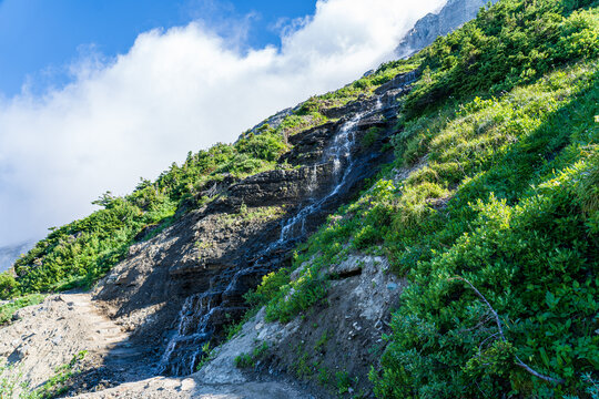 Waterfall crossing the hiking path on the Highline Trail in Glacier National Park on a sunny summer dya