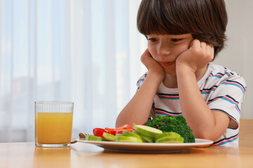 Cute little boy refusing to eat vegetables at home