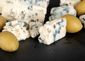 Cheese with blue mold and green olives isolated on a black background. Close-up.