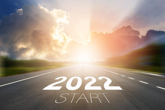 Start to New year 2022 concept. Start 2022 written on highway road in the middle of empty asphalt road with sunset or sunrise light above asphalt road.
