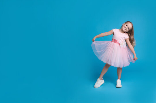Cute little girl in beautiful dress dancing on light blue background. Space for text