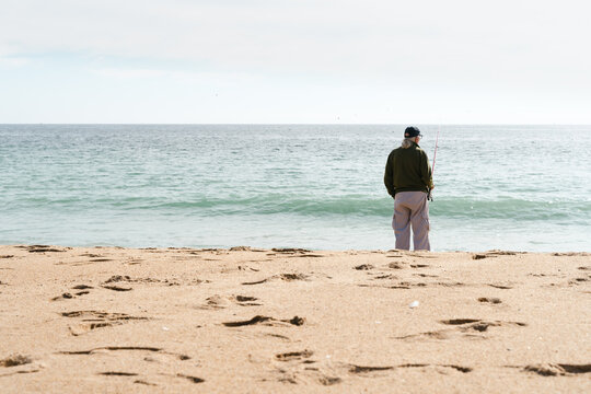 Lonely senior man fishing on the beach. Elder person enjoying retirement by the sea concept