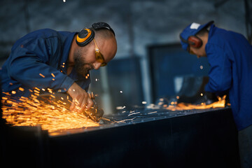 Side view of two young worker in special dark blue uniform and headphone polishing or creating...