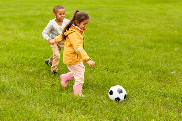 childhood, leisure games and people concept - happy little boy and girl with ball playing soccer at summer park