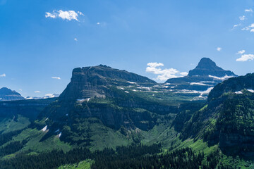 View from Logan Pass in Glacier National Park, Montana on a sunny summer day, with glacial valley, snow-capped mountains, alpine lakes, and grass