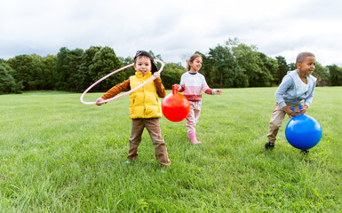 childhood, leisure and people concept - group of happy children playing with hopper balls and hula hoop at park