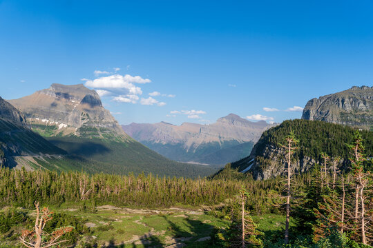 View from Logan Pass in Glacier National Park, Montana on a sunny summer day, with glacial valley, snow-capped mountains, alpine lakes, and grass